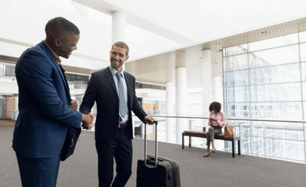 two business men walking and shaking hands with a suitcase in the other hand.