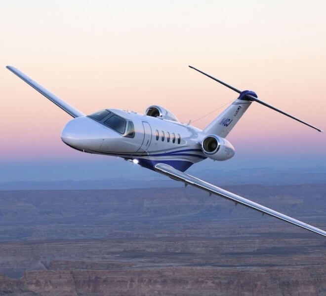 private jet flying in the air with a pink sky in the background