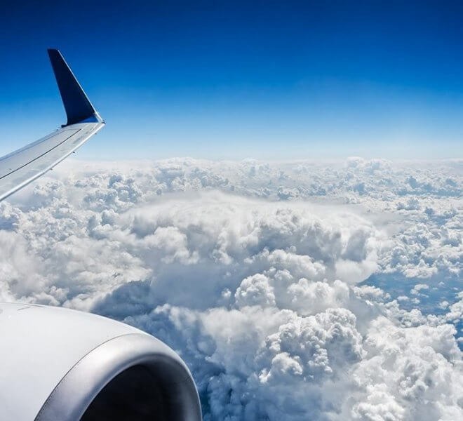 View looking out of plane window with top of clouds, plane wing, and turbine.